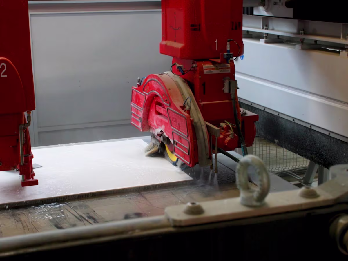 Red industrial machine cutting a white stone slab in a production facility.