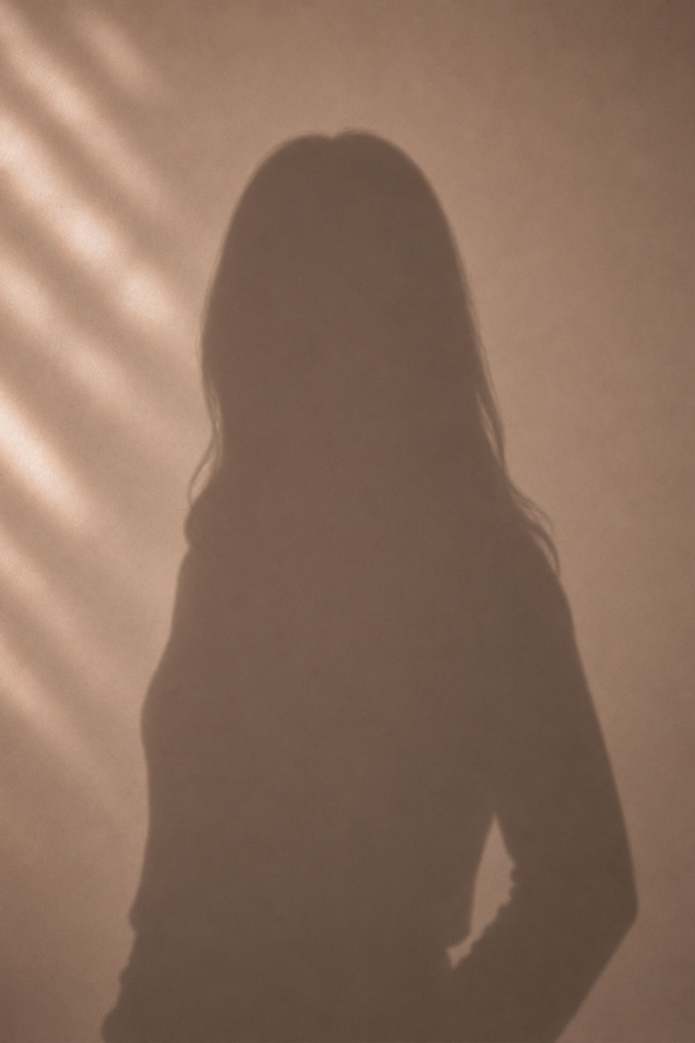 Schatten einer Person mit langen Haaren vor einer Wand mit Lichtstreifen.