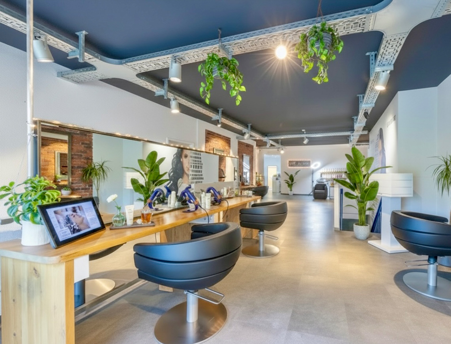Moderner Friseursalon mit schwarzen Stühlen, Holzarbeitsplatz, Spiegeln und grünen Pflanzen.