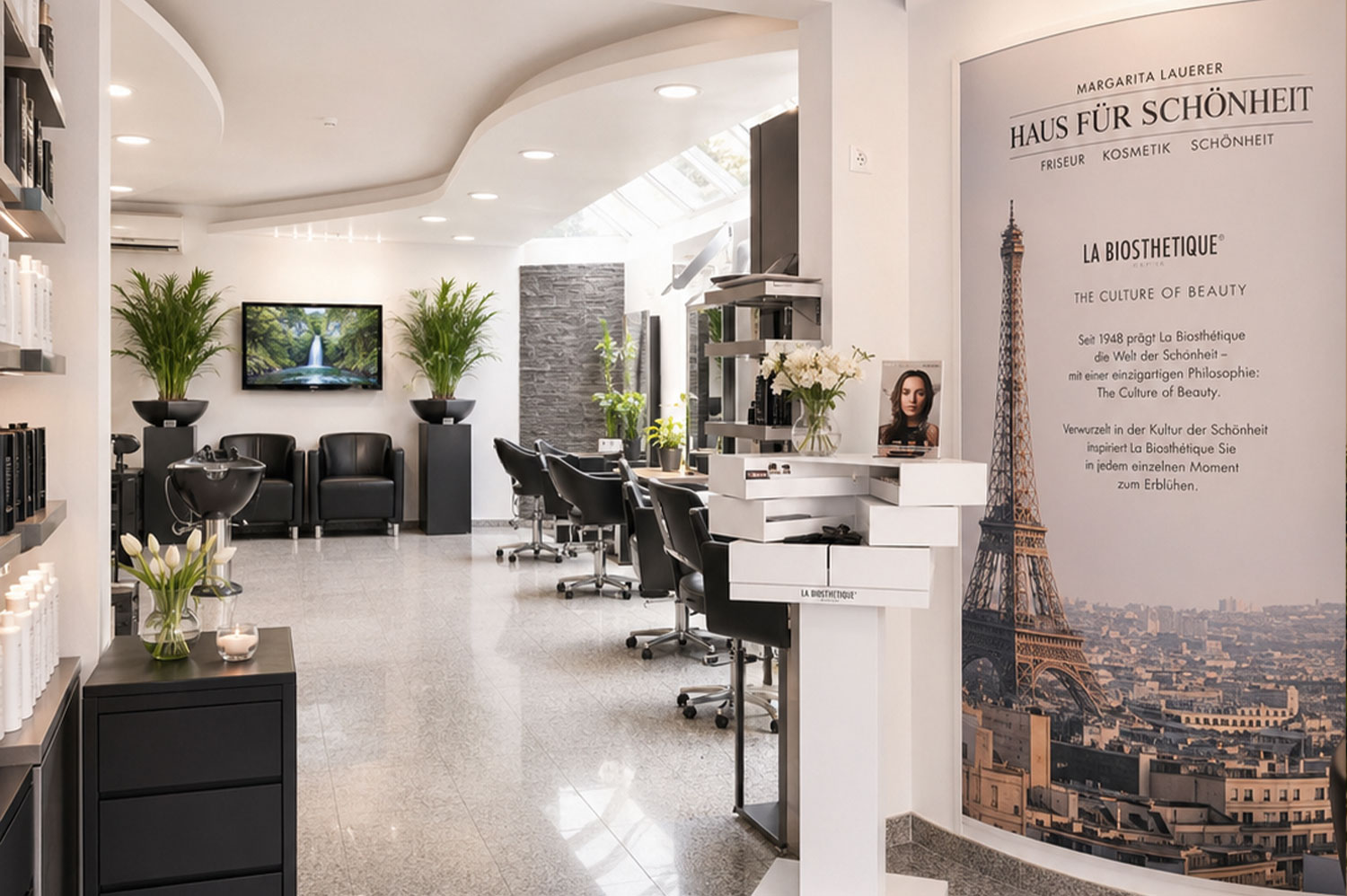 Modern beauty salon with black chairs, plants, product shelves, and a large Eiffel Tower poster.