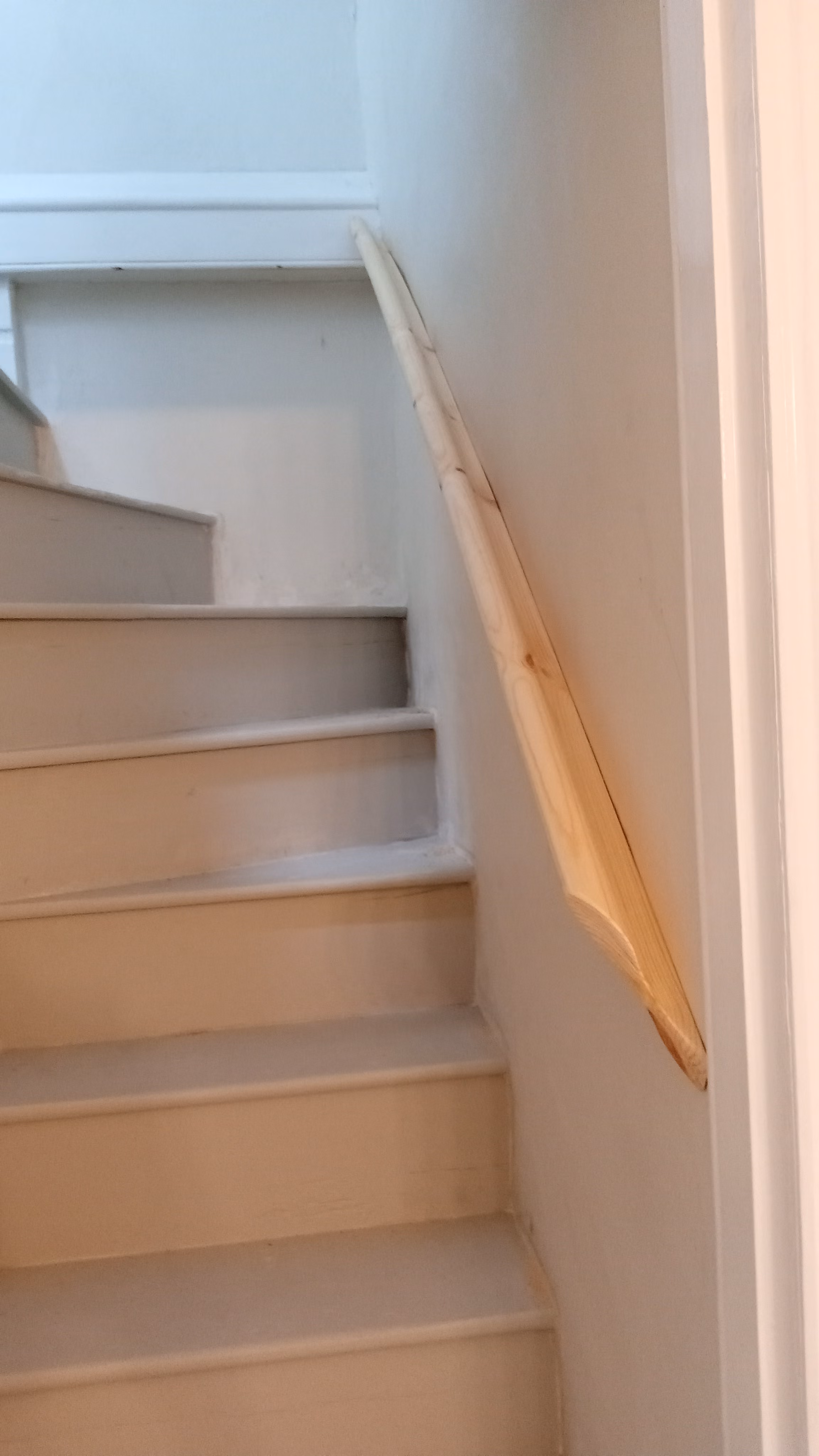 Indoor staircase with white steps and a wooden handrail attached to the right wall leading upward.
