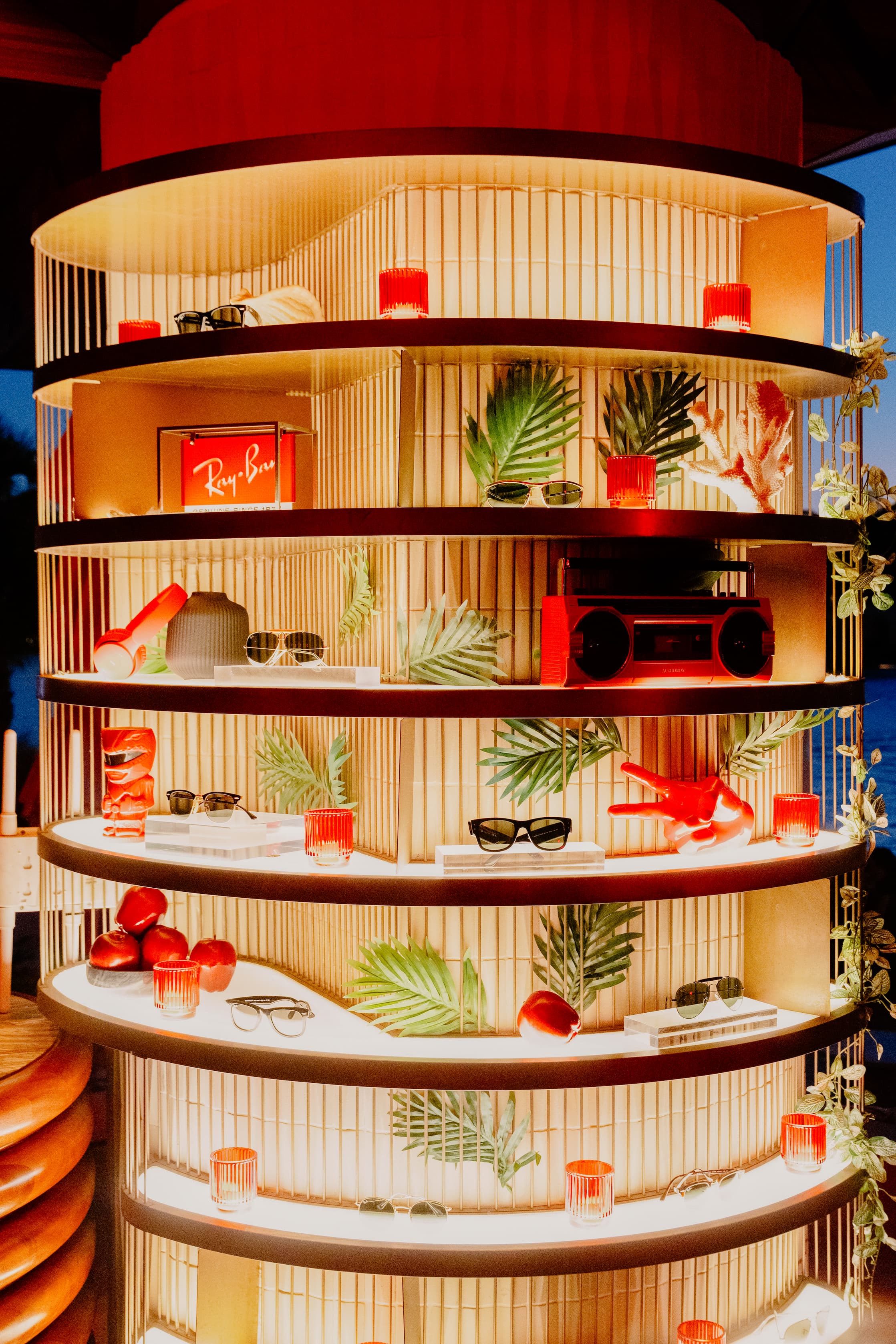 tiki inspired bar shelf featuring retro red radios, red tiki glasses, ray-ban signs, sunglasses, illuminated at dusk for a private event