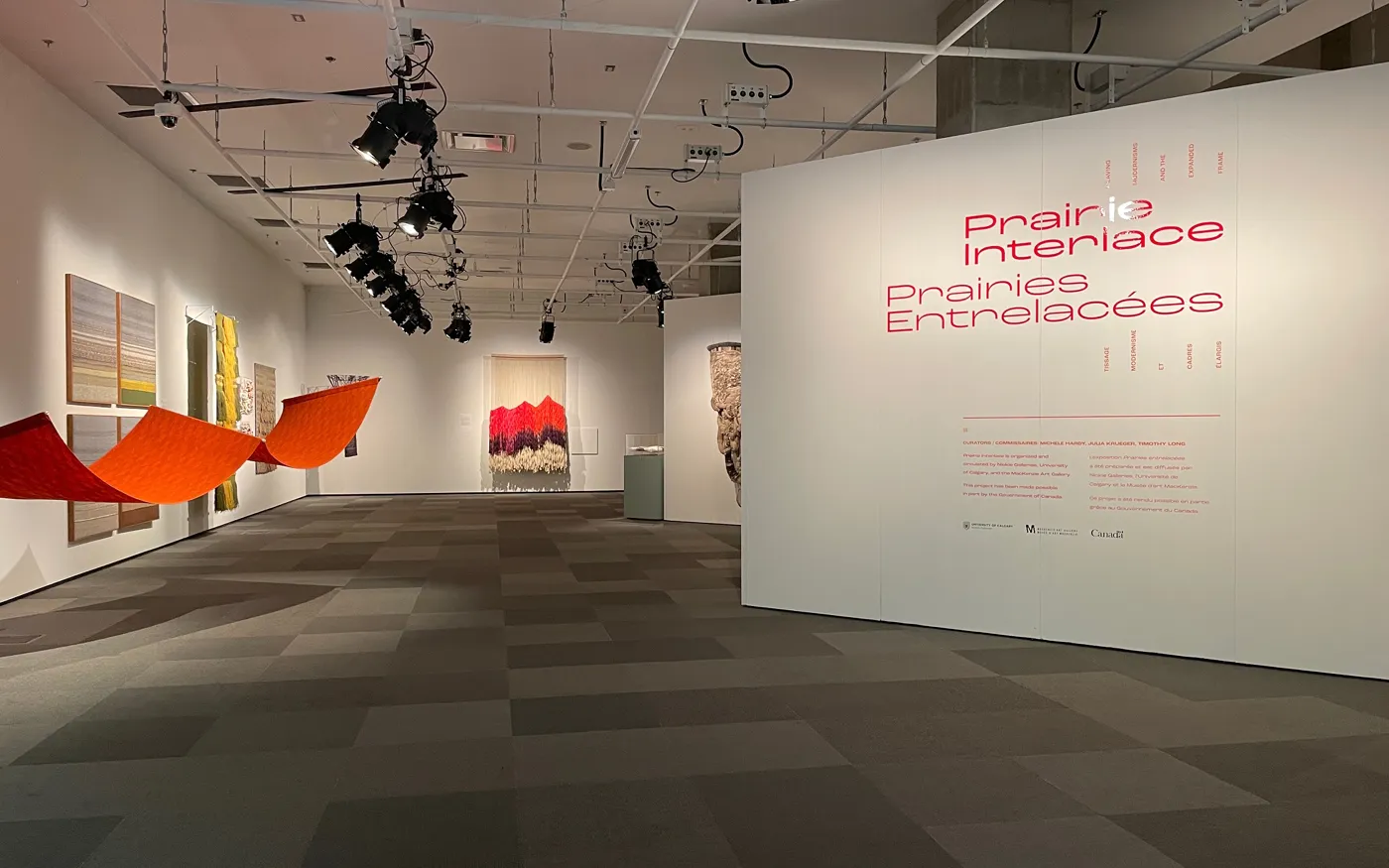 UCalgary Nickle Galleries — Prairie Interlace exhibition intro panel with textile artworks on display