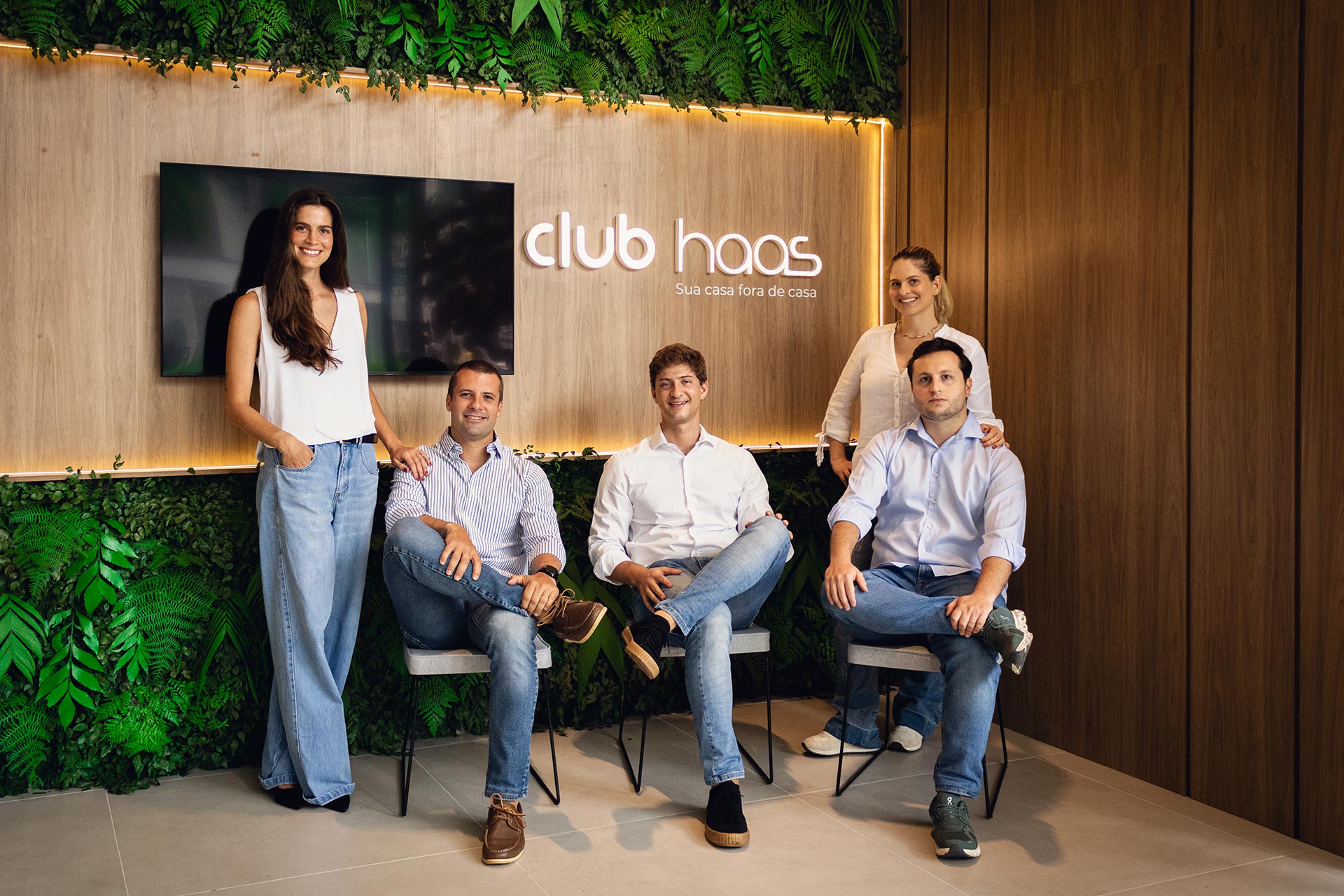 Equipe do Club Haas sentada em frente ao painel com a marca