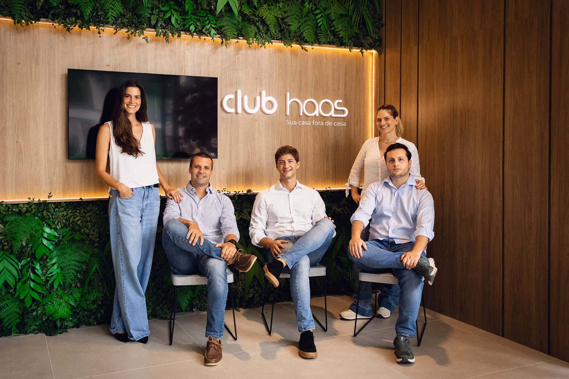 Equipe do Club Haas sentada em frente ao painel com a marca