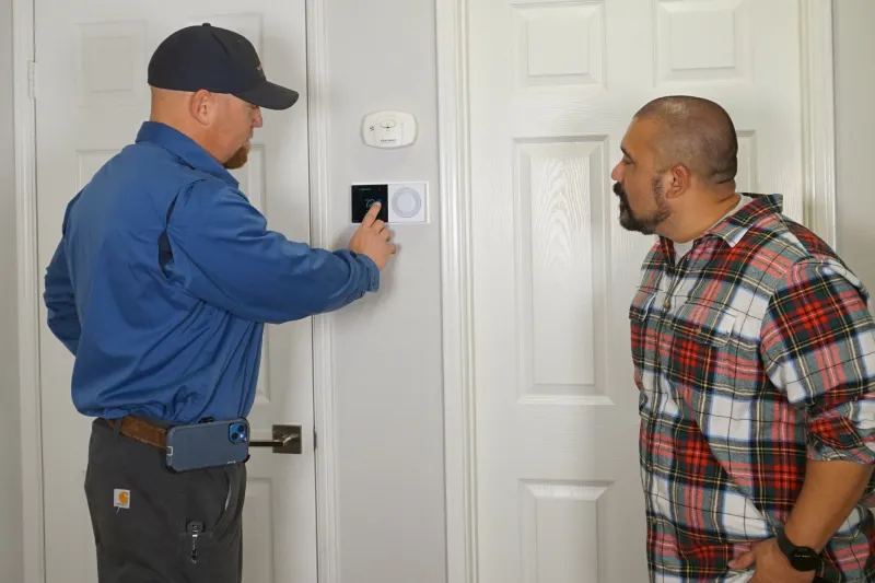A tech showing new thermostat options on the thermostat to a customer.