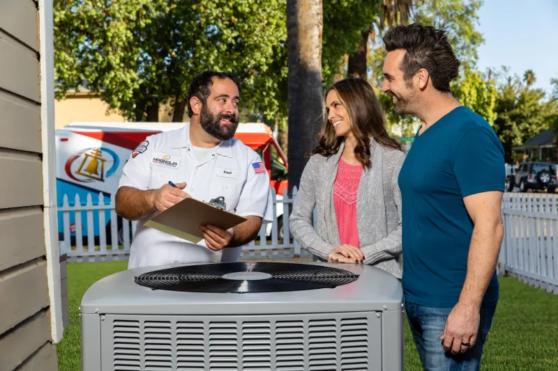A tech talking to customers about their options in front of an AC unit.