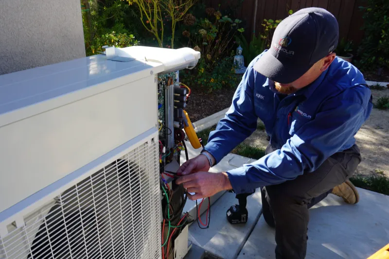 A tech working on a heat pump outside of a home.