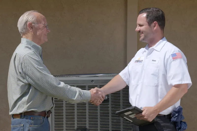 A tech shaking the hand of a customer in front of an AC unit.