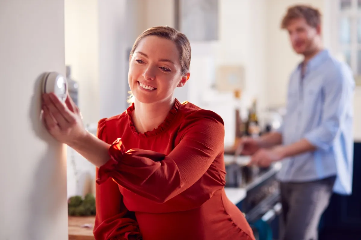 A woman changing the thermostat in her home.