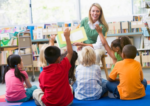 Teacher reading a picture book to young students in library