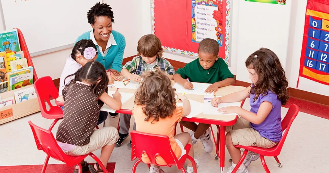 Teacher smiling while guiding young students drawing at classroom table