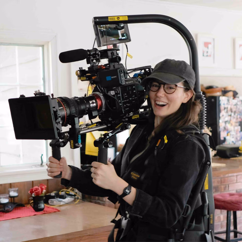 Smiling camera operator holding a shoulder-mounted cinema camera rig indoors