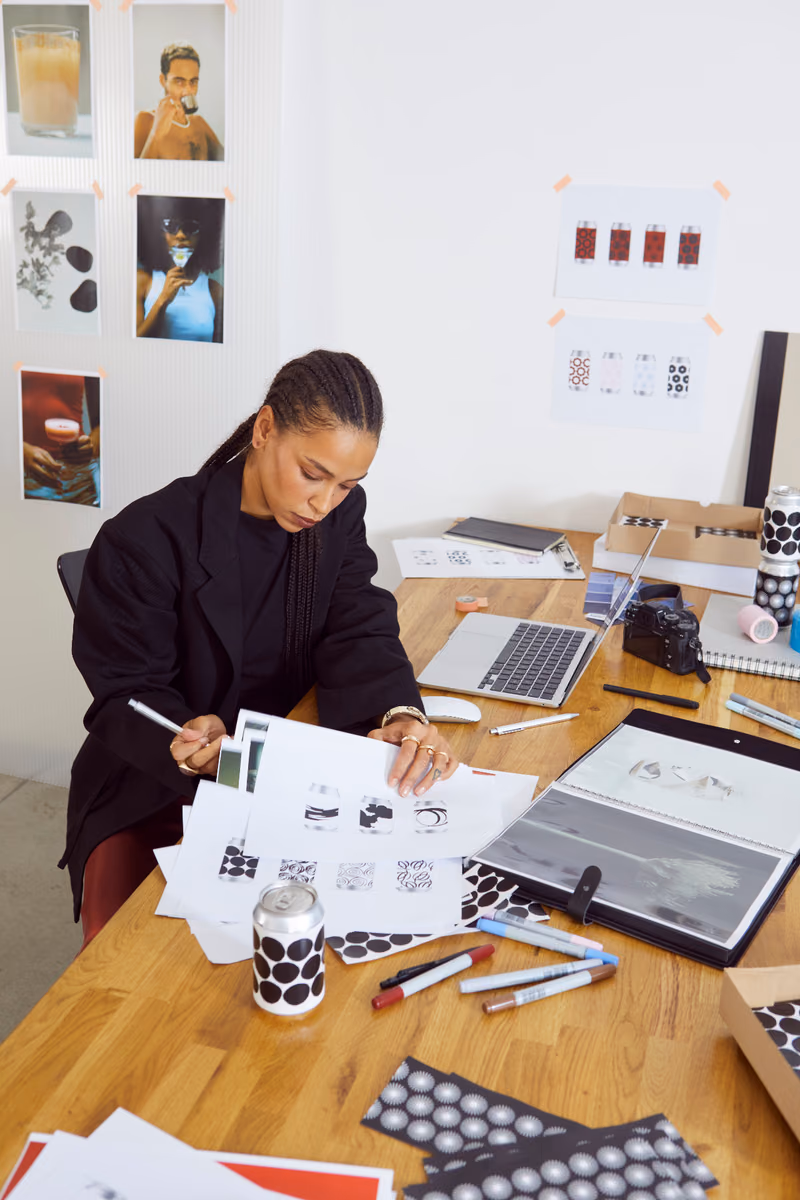 Designer reviewing printed packaging concepts at a desk covered with samples and markers