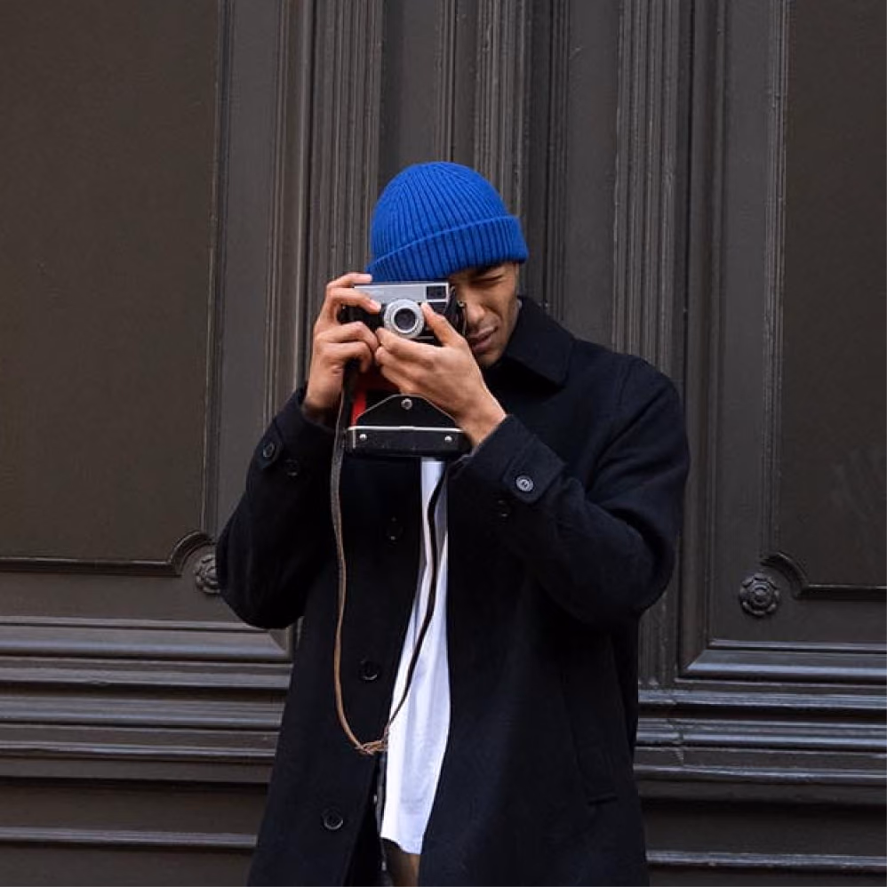 Photographer in a blue beanie shooting with a film camera in front of a dark panelled door