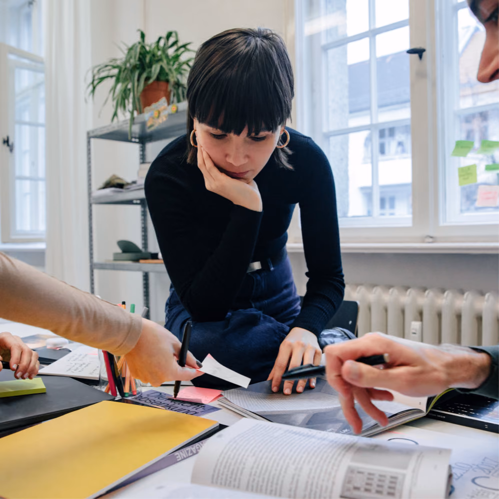 Team gathered around a table covered with printed pages, sticky notes and colour swatches