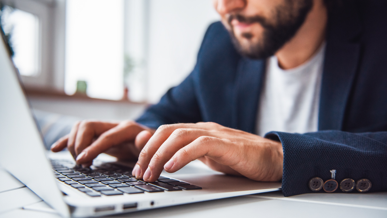 A close up of a man in a business setting typing in a laptop computer