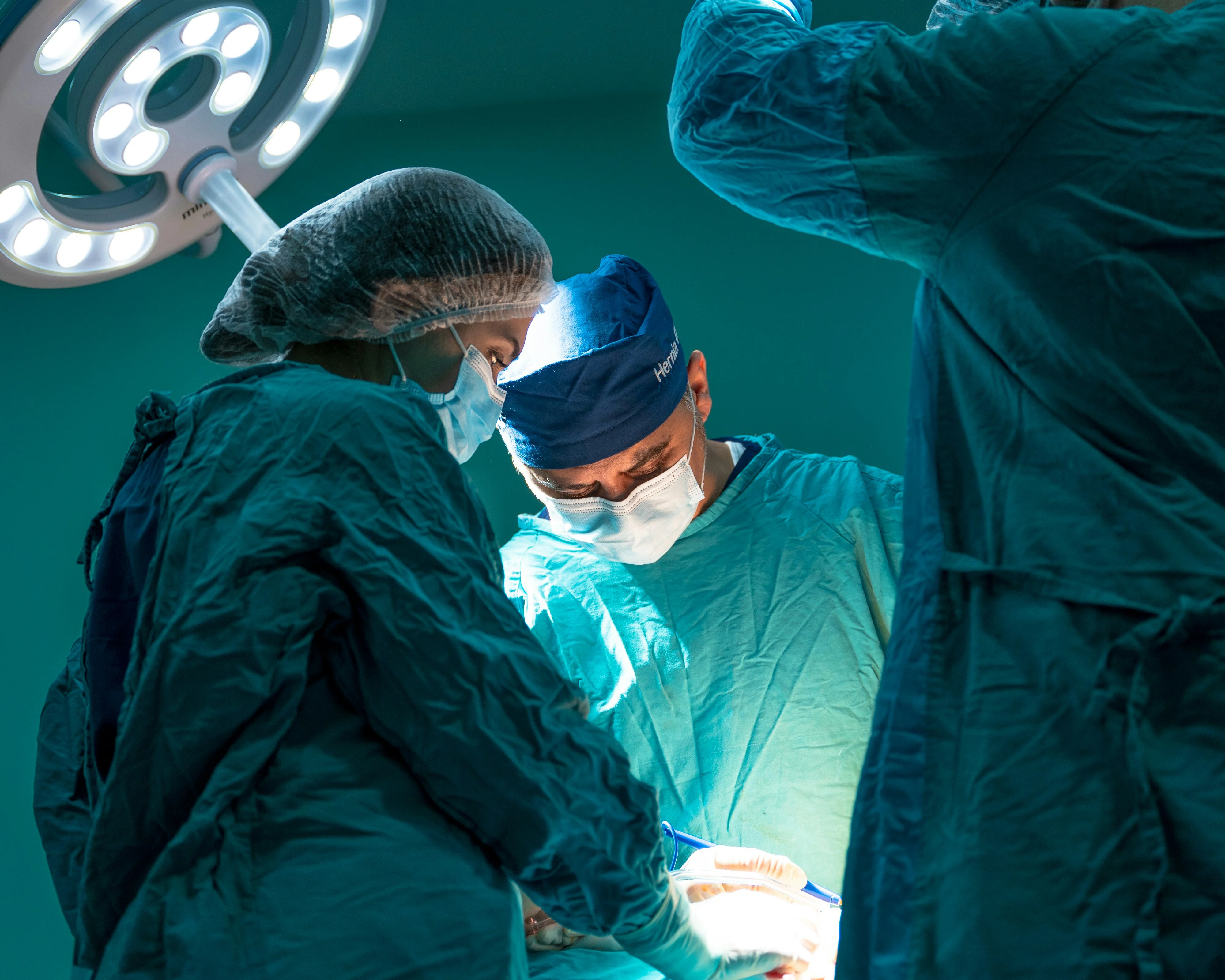 Surgical team in scrubs and masks operating under an overhead surgical light