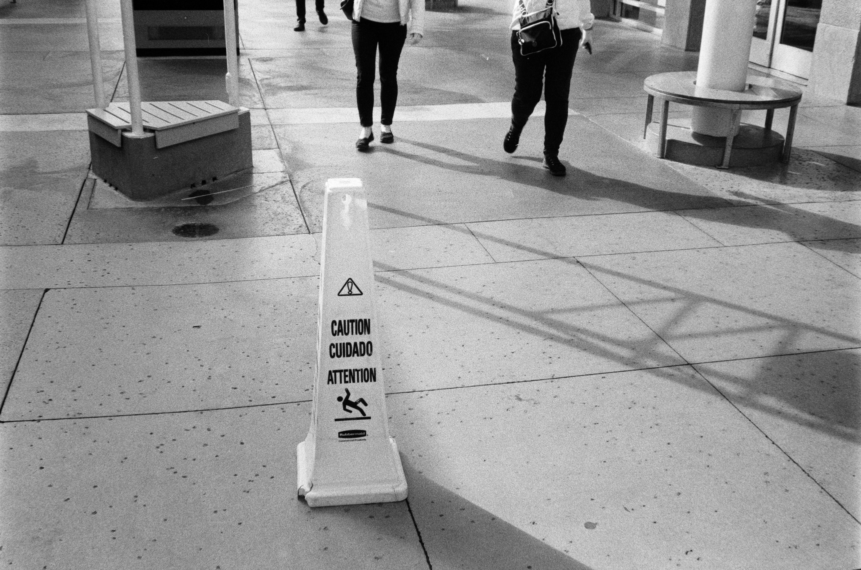 A wet floor caution sign on a walkway with people passing