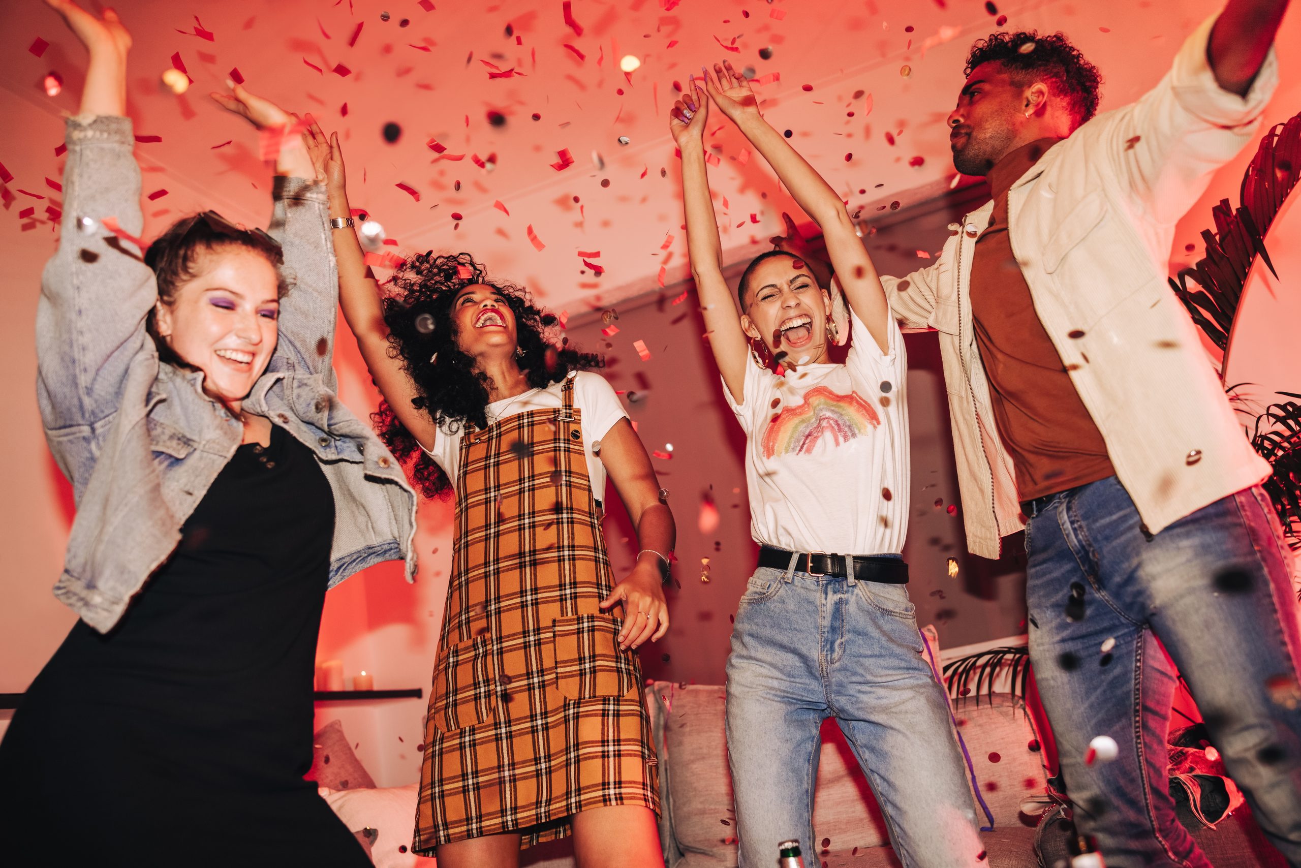 Friends outdoors with their arms raised as confetti falls around them