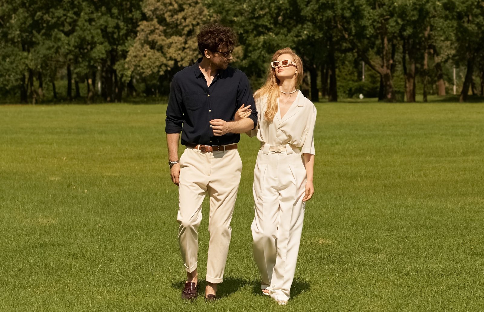 A couple walking arm in arm across a sunny park lawn