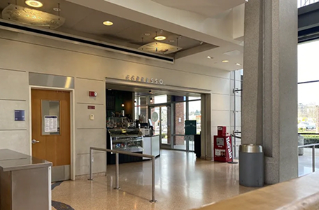 Interior view of a modern café named Espresso inside a building with a tiled floor, stainless steel trash can, wooden door, and glass entryways.
