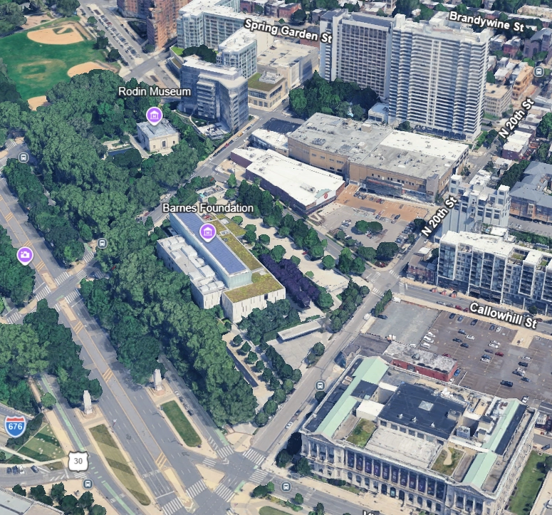 Aerial view of an urban area showing the Barnes Foundation and Rodin Museum surrounded by dense green trees, nearby streets labeled including Spring Garden St, Brandywine St, N 20th St, and Callowhill St, with surrounding buildings and a visible park with baseball fields.