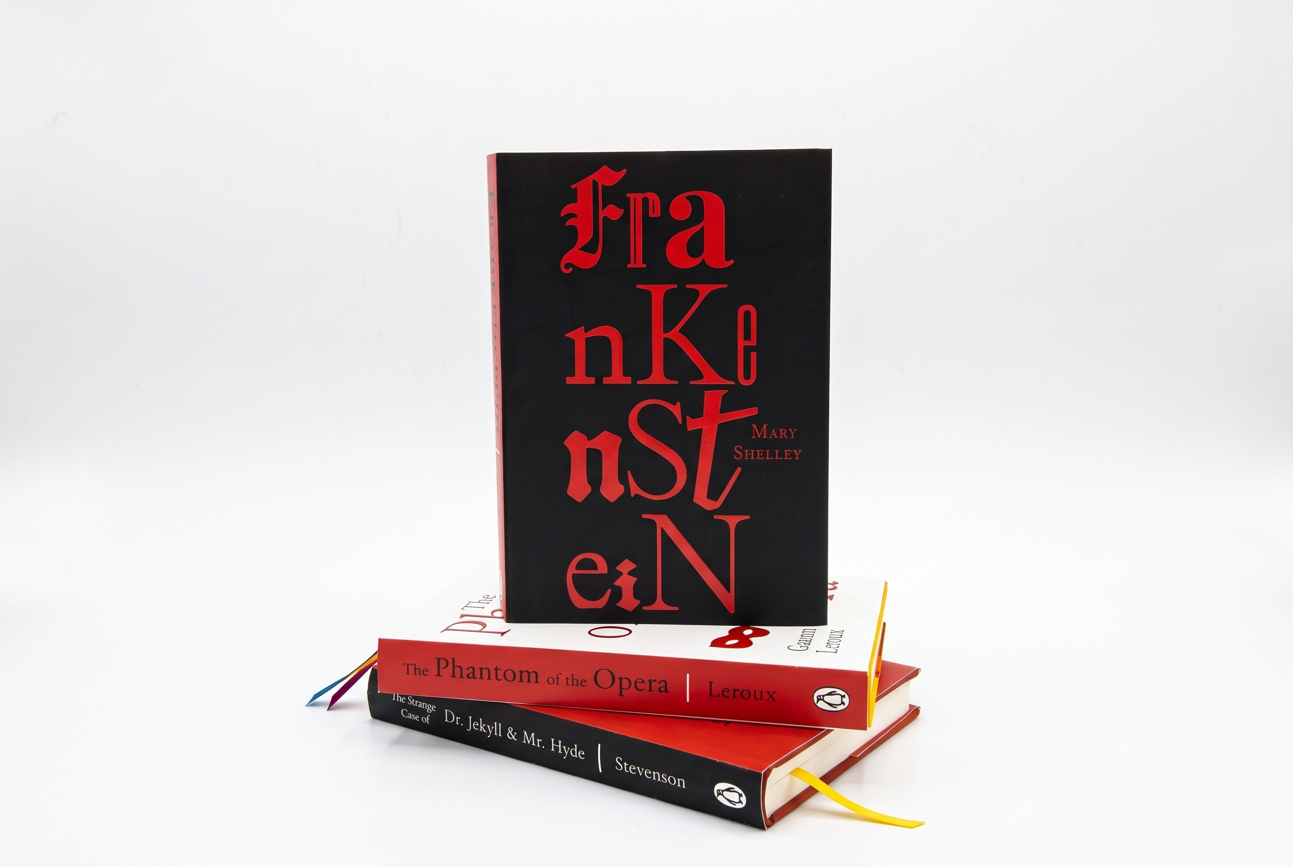 Stack of three classic novels, with Frankenstein by Mary Shelley standing upright on top of The Phantom of the Opera by Leroux and The Strange Case of Dr. Jekyll & Mr. Hyde by Stevenson, all with distinctive cover designs.