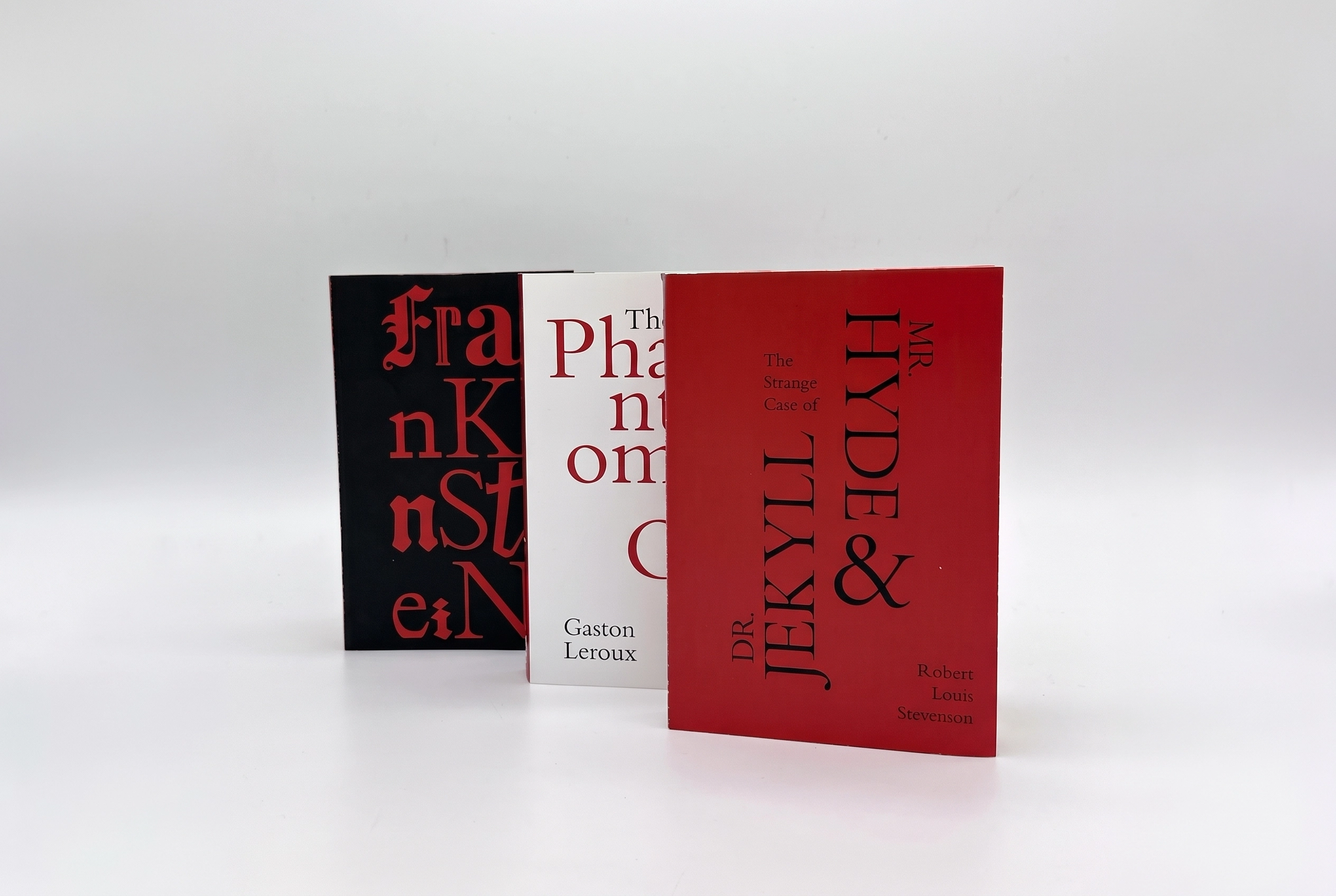 Three classic novels standing upright side by side: 'The Strange Case of Dr. Jekyll & Mr. Hyde' by Robert Louis Stevenson with a red cover, 'The Phantom of the Opera' by Gaston Leroux with a white cover, and 'Frankenstein' with a black cover and red text.