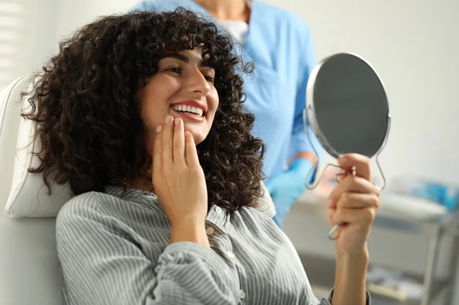 woman smiling and looking at her smile in the mirror