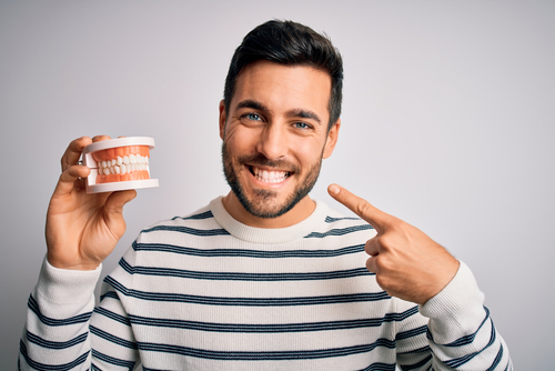 man pointing at his smile and holding a model of a mouth