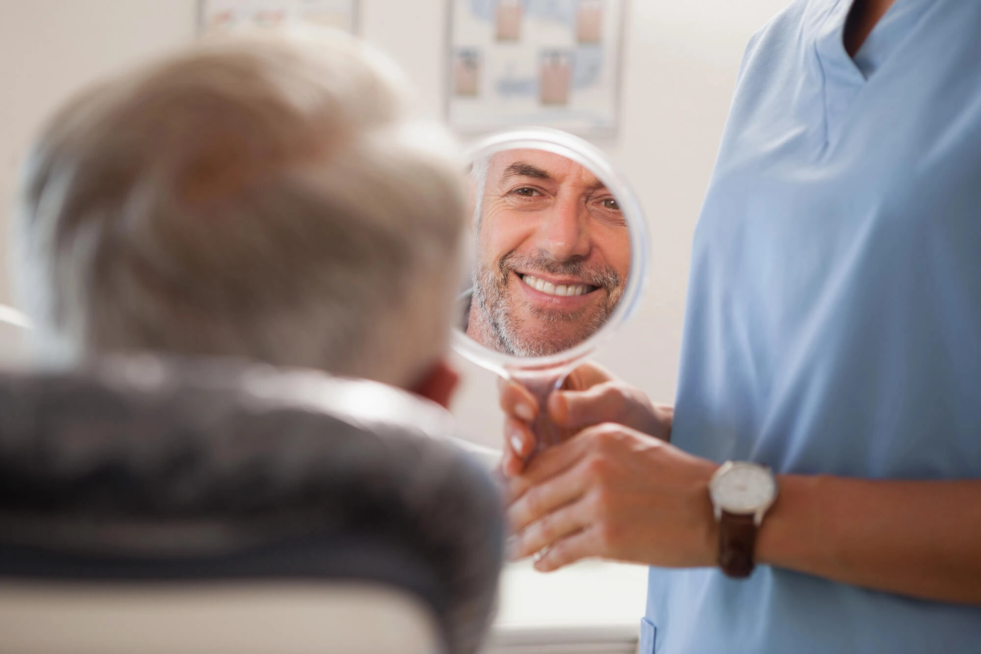 man smiling and looking at his smile in the mirror