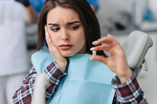 woman with dental pain holding her tooth at the dentist
