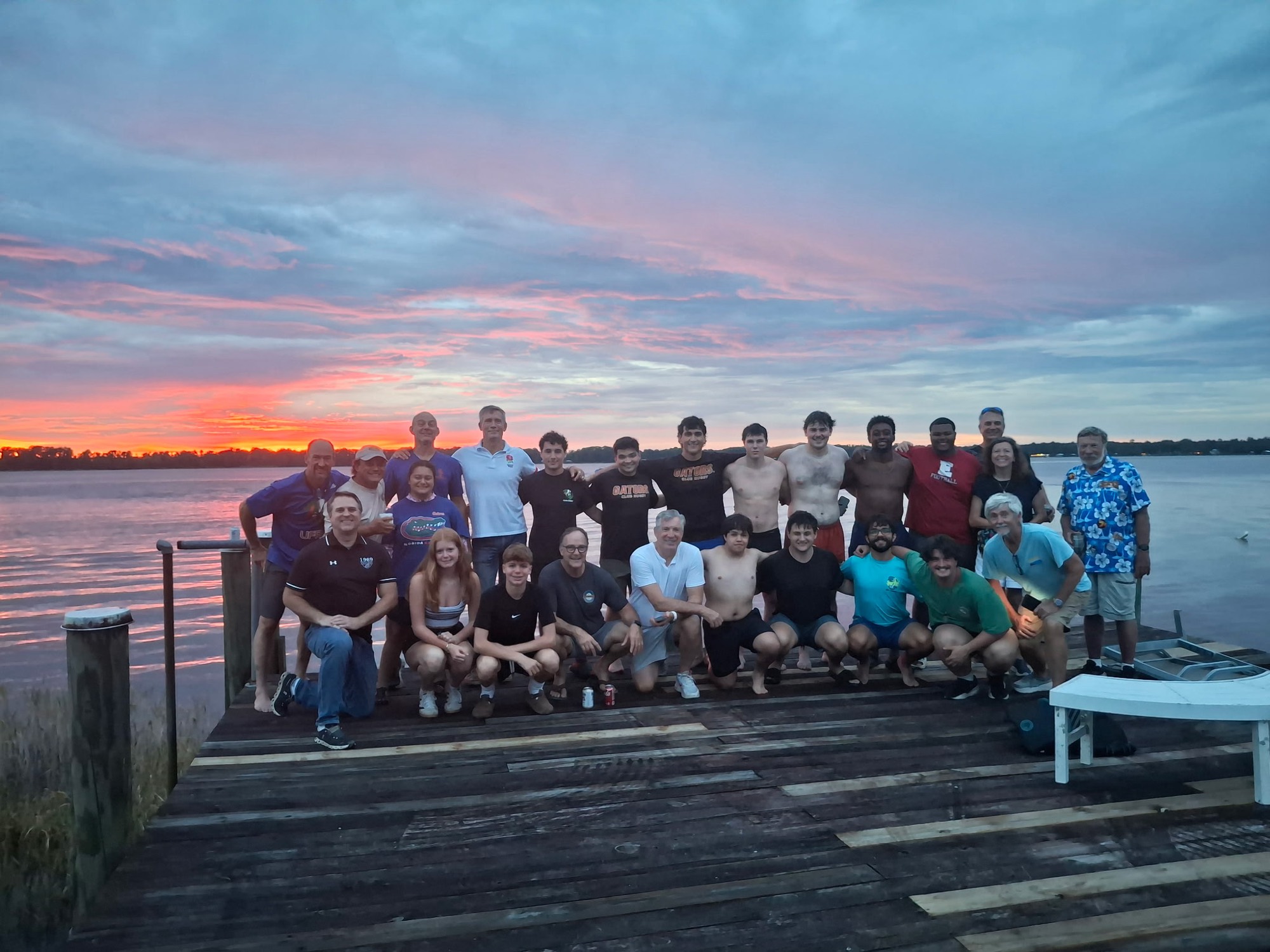 Players, alumni, and families gathered on the dock at UF Rugby Haven at sunset
