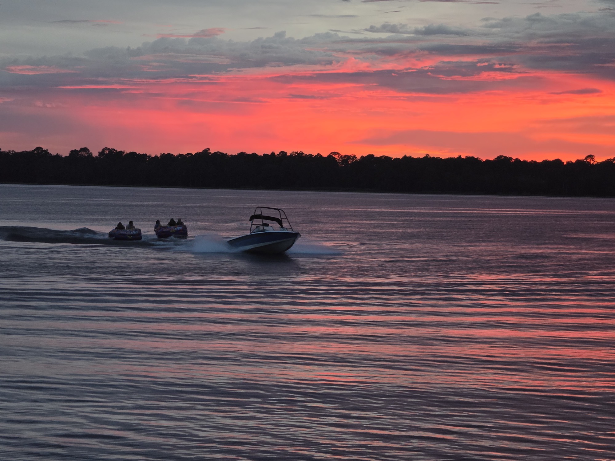 A boat pulls two tubes across the water at sunset during Lake Day