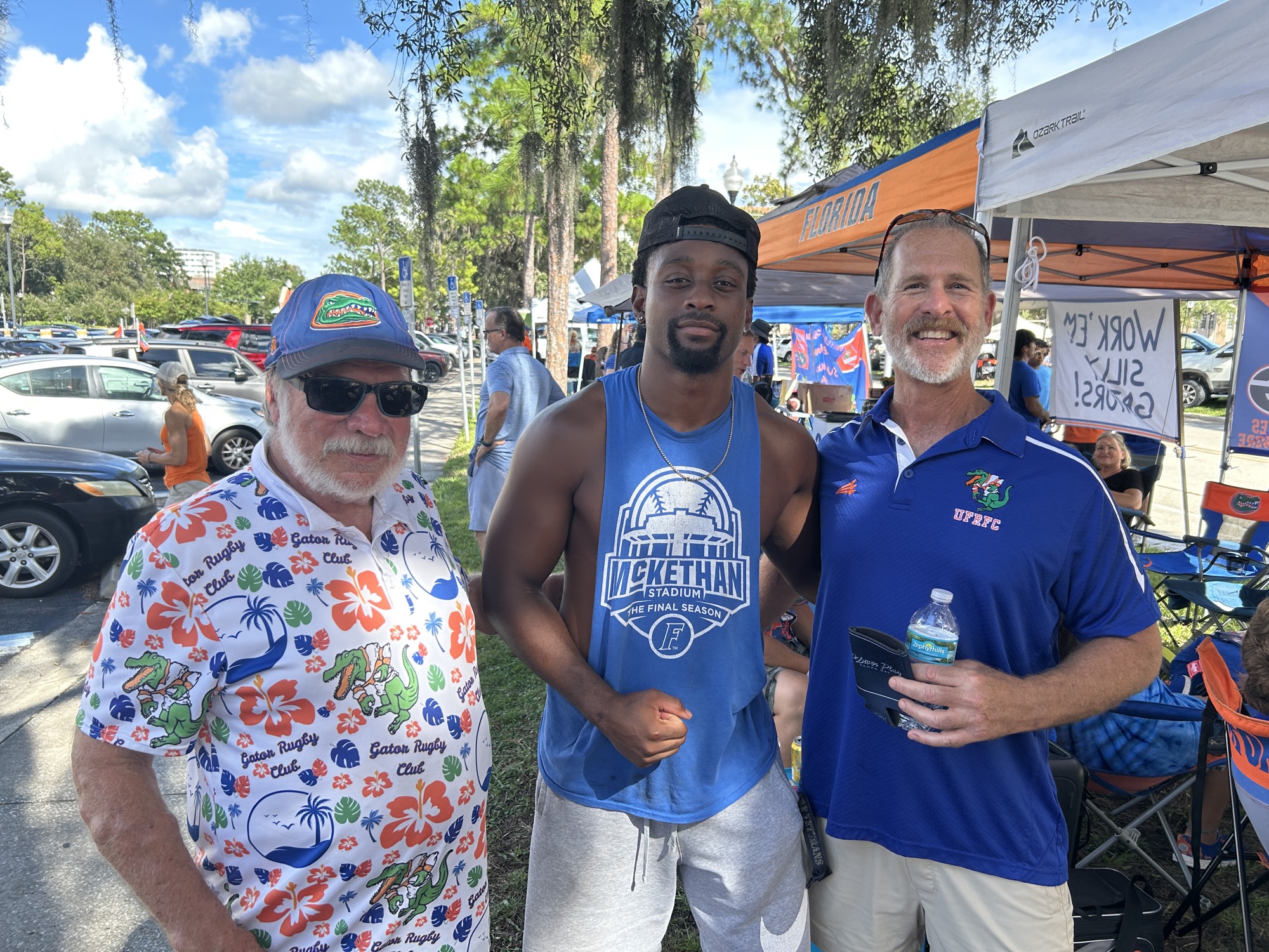 Two Gator rugby alumni stand with a current player at the tailgate