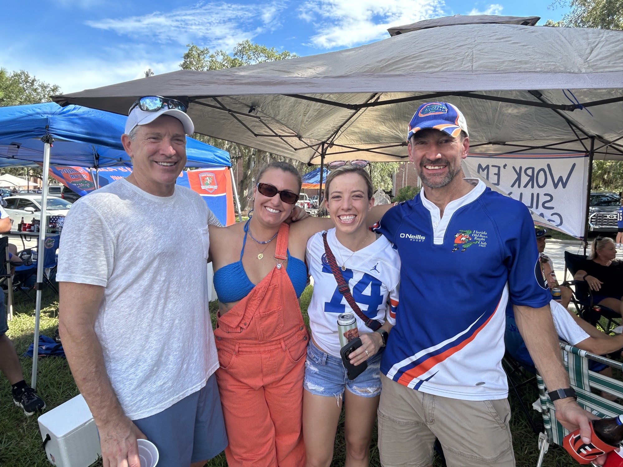 Four supporters in Gators gear under a tailgate tent on Union Road