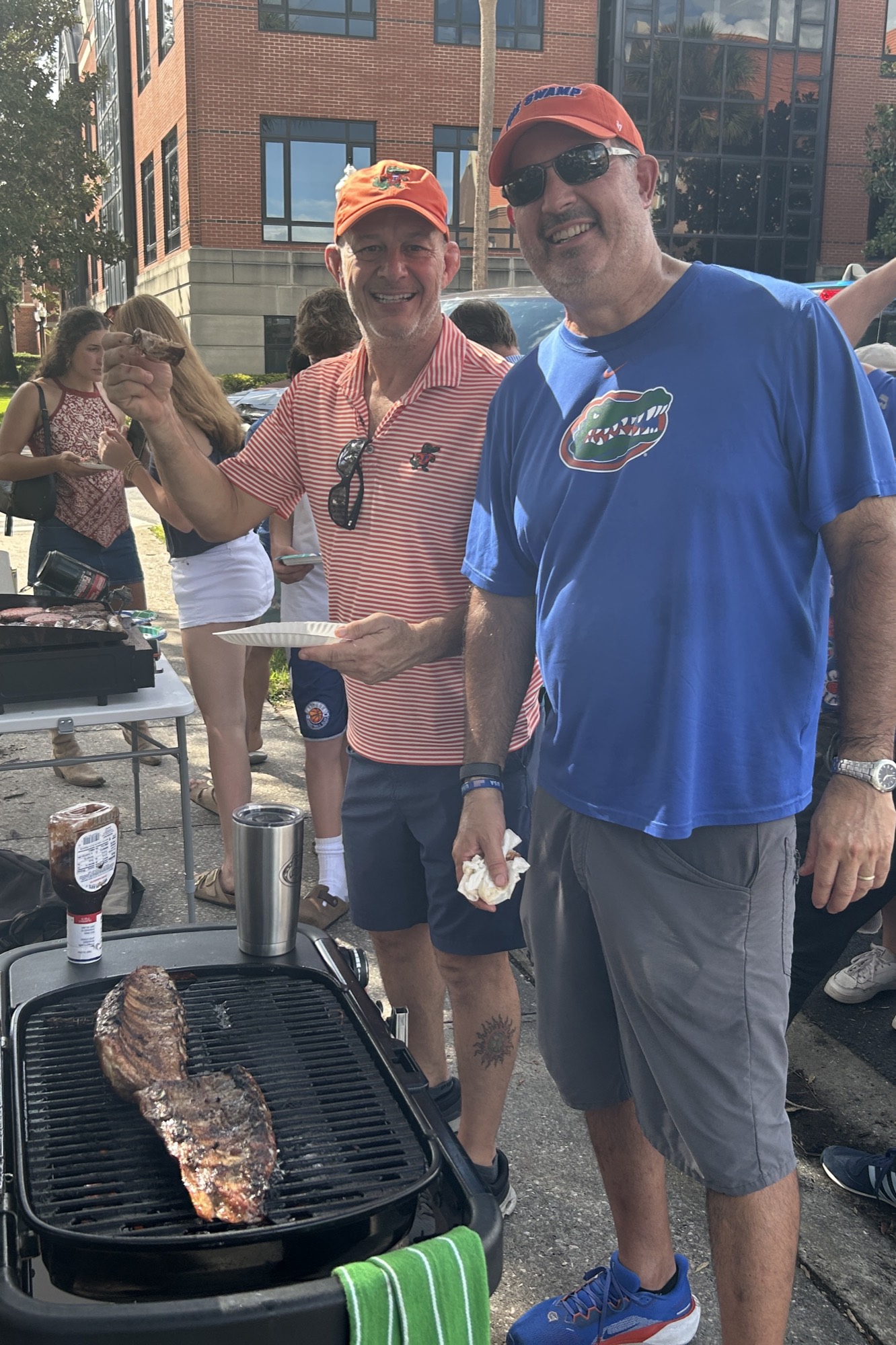 Two Gators supporters stand over a grill with a rack of ribs