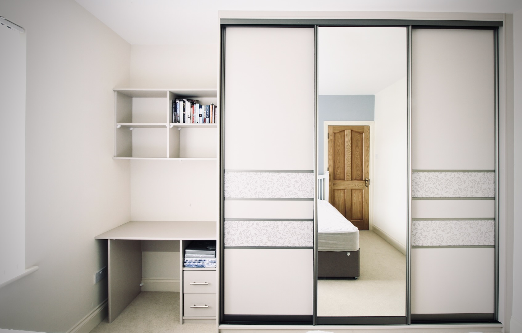 Kids' fitted wardrobe with three sliding doors including a full-length mirror and patterned glass details. Includes a built-in desk with a drawer unit and wall-mounted shelving for books and study essentials.