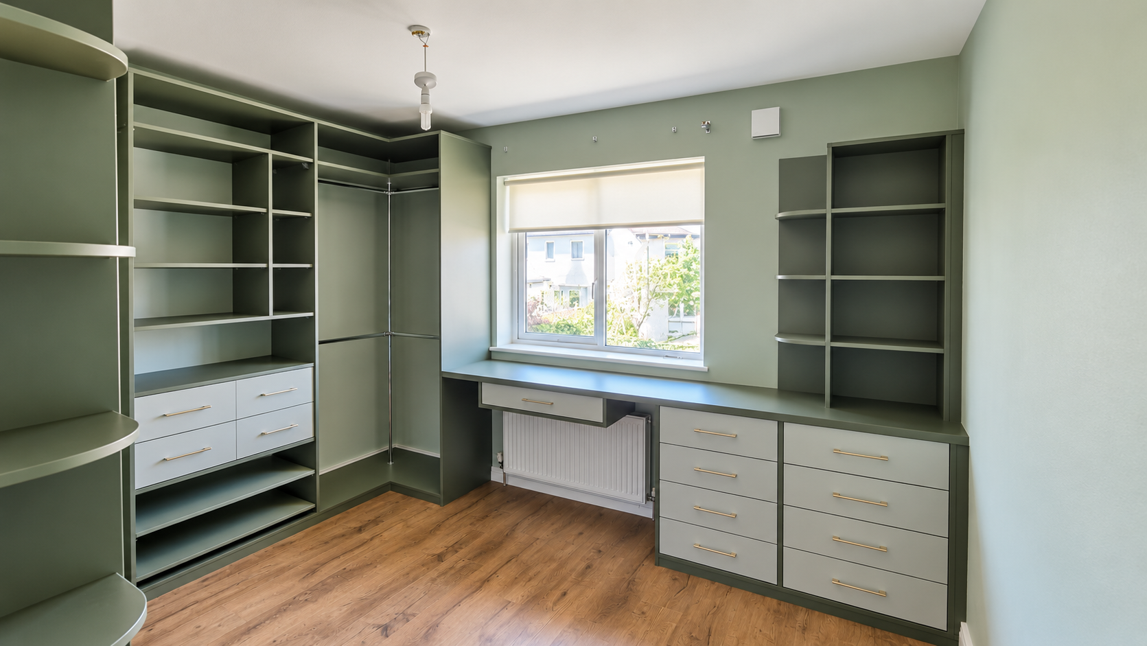 Sage green fitted wardrobe and desk unit with open shelves, hanging rails, and soft-close drawers. Modern bedroom storage solution with custom cabinetry and gold handles.