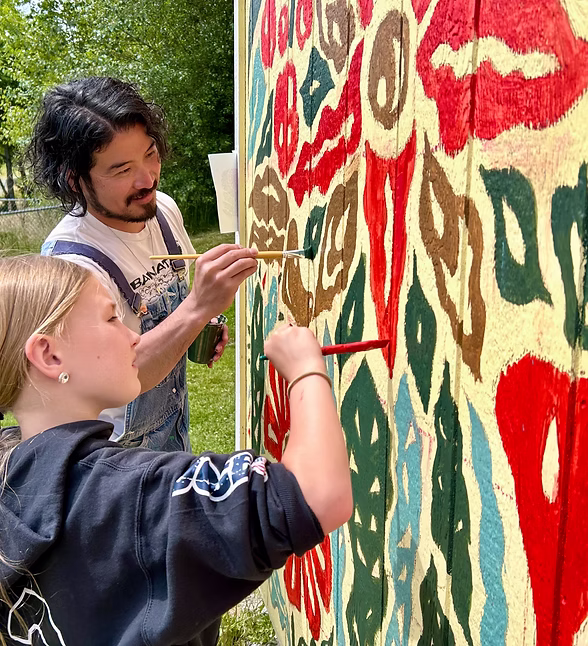 Two people painting colorful patterns on a wall outdoors on a sunny day.