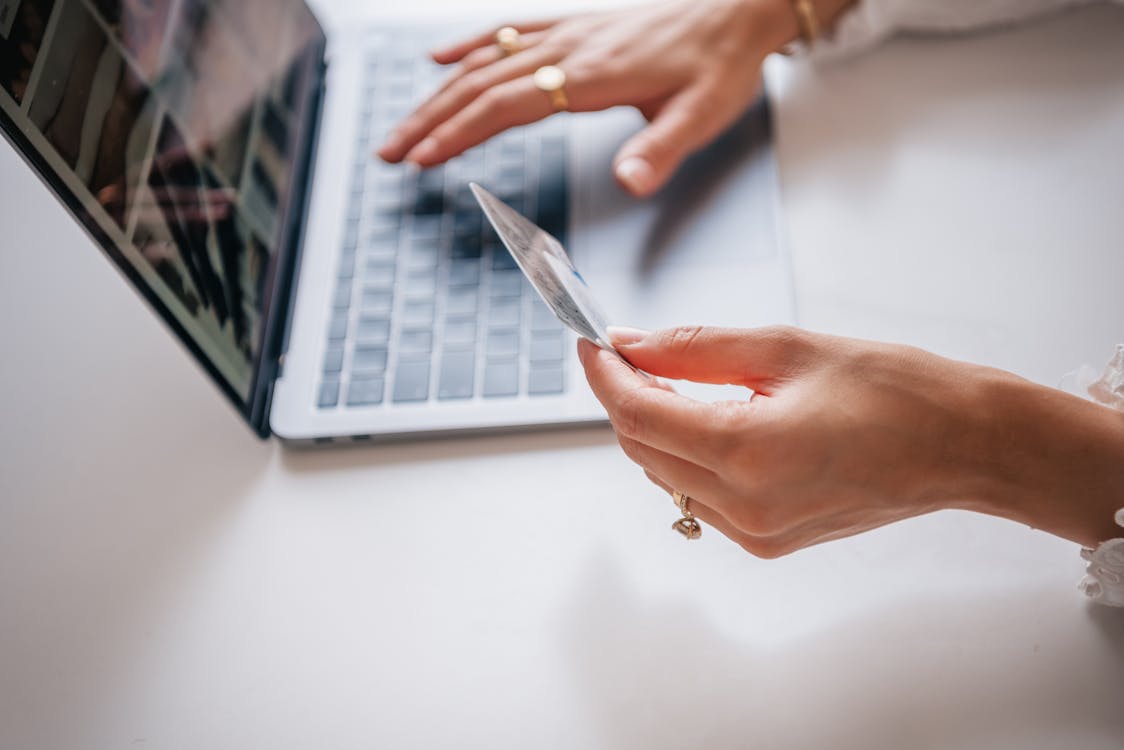 Free Close-up of woman holding a credit card while typing on a laptop, representing online shopping. Stock Photo