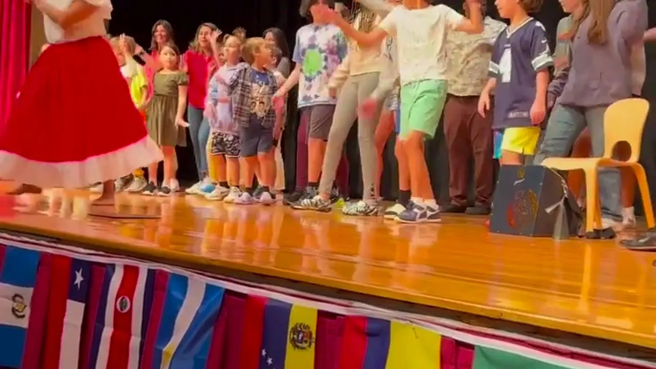 Students performing on stage in front of a row of flags at a school assembly
