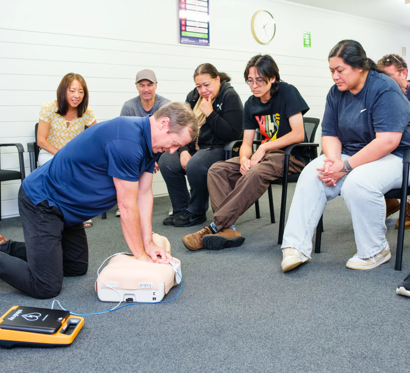 MediTrain instructor demonstrating CPR with an AED to a seated workplace group