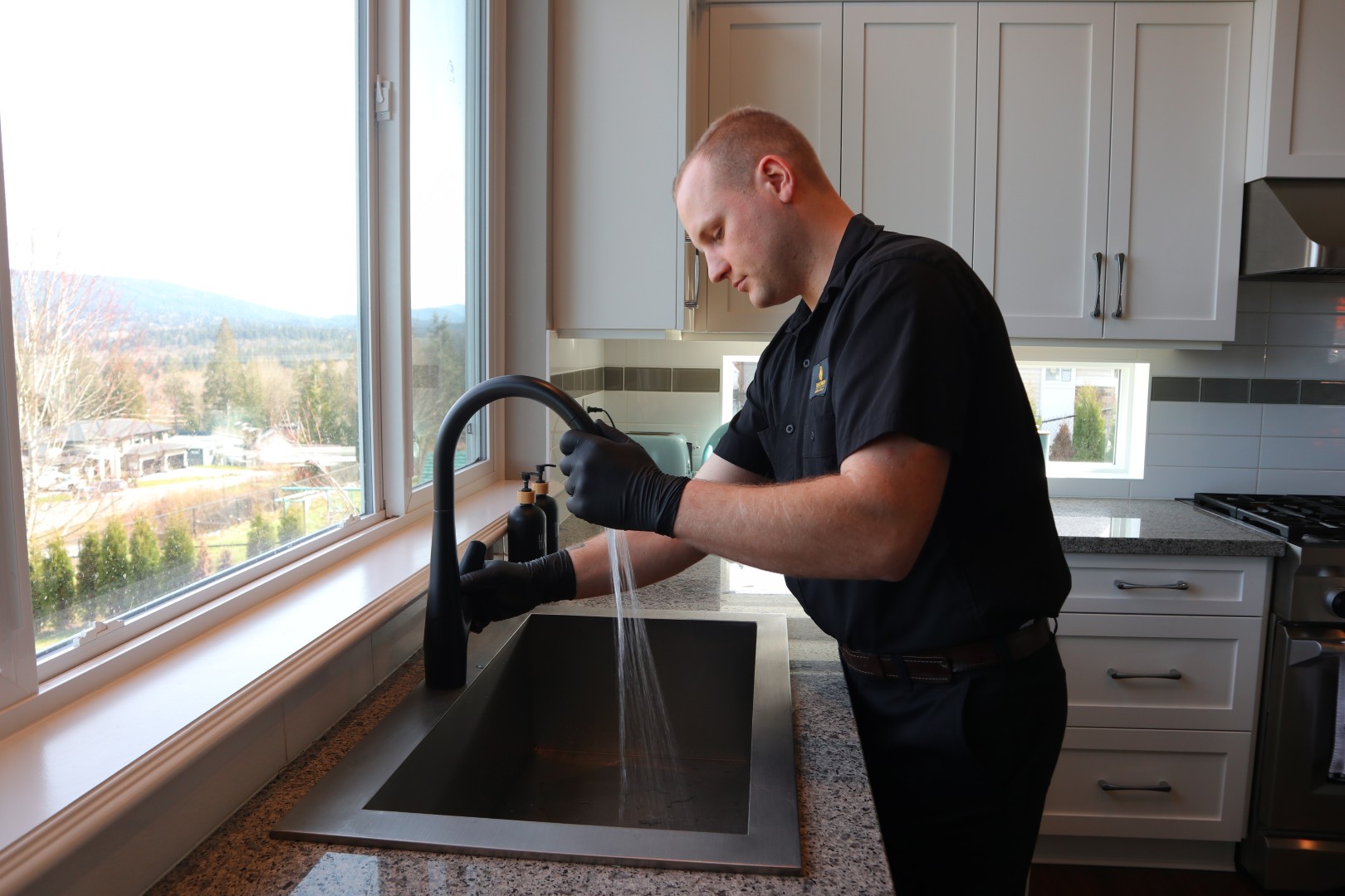 A Crazy Plumber technician in gloves testing the water flow of a black pull-down kitchen faucet.