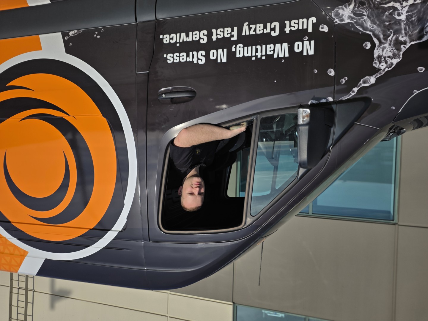 A Crazy Plumber technician smiling from the driver's window of the company's branded service van.