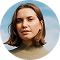 Portrait of a woman with shoulder-length brown hair wearing a brown sweater against a clear sky.