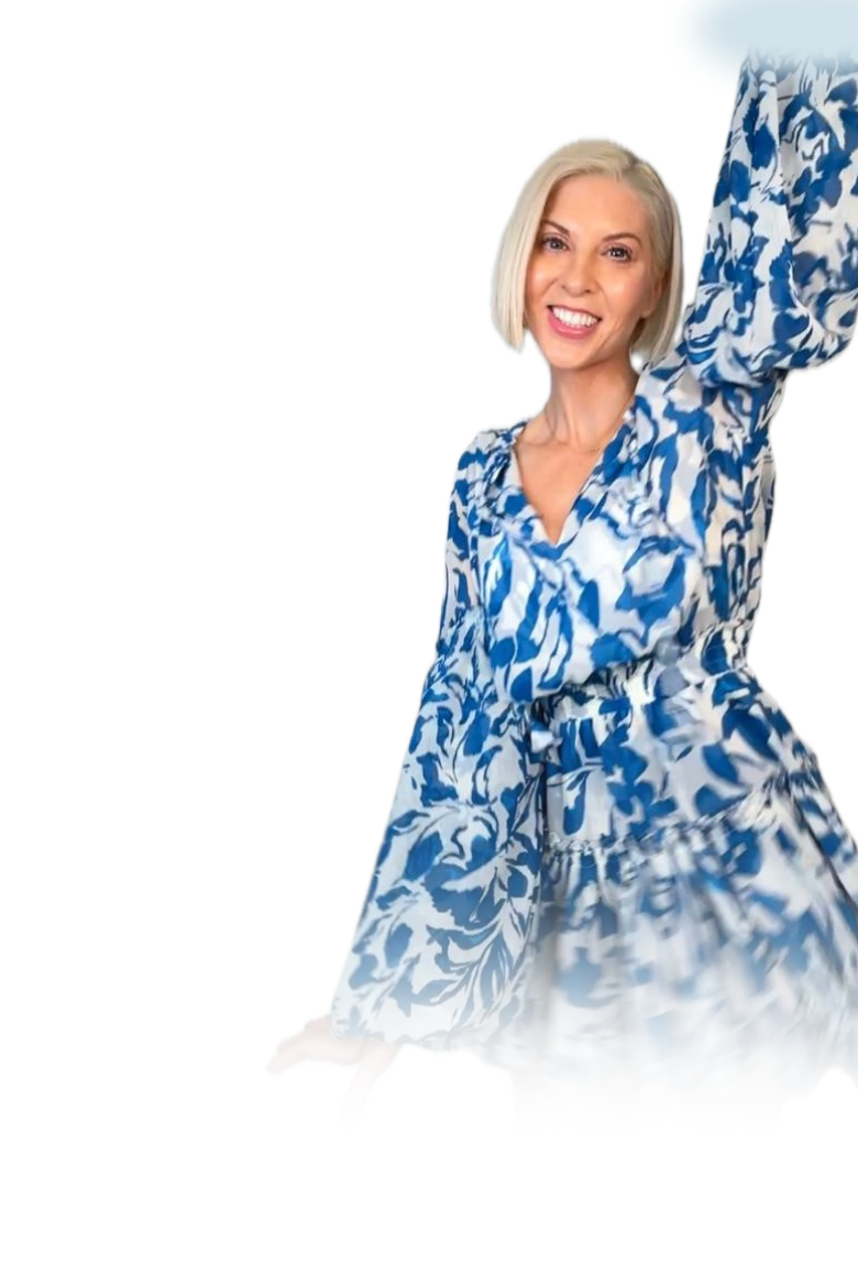 Smiling woman with short blonde hair wearing a blue and white floral dress raising one arm.