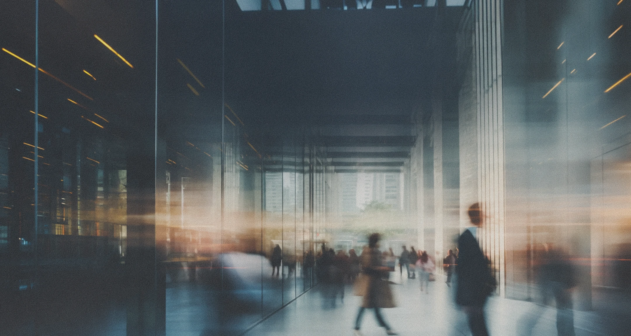 Blurred motion scene of people walking through a modern glass and concrete urban building corridor with reflections and soft lighting.