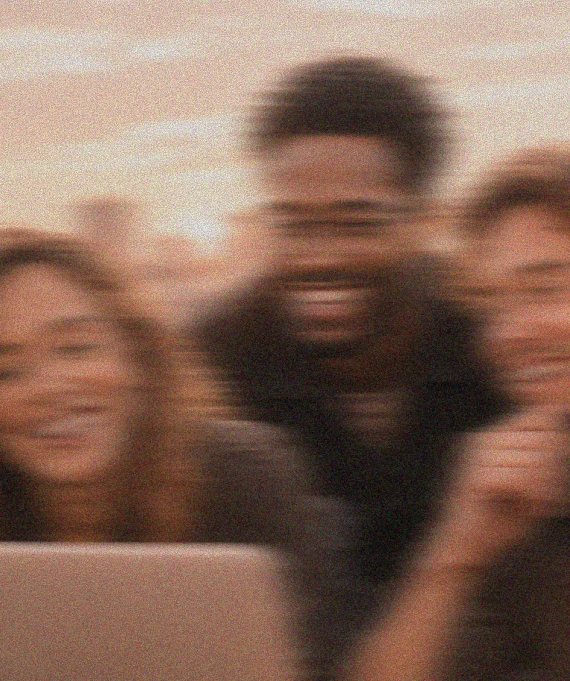 Blurry photo of three people smiling and gathered closely, seemingly looking at a laptop screen together.